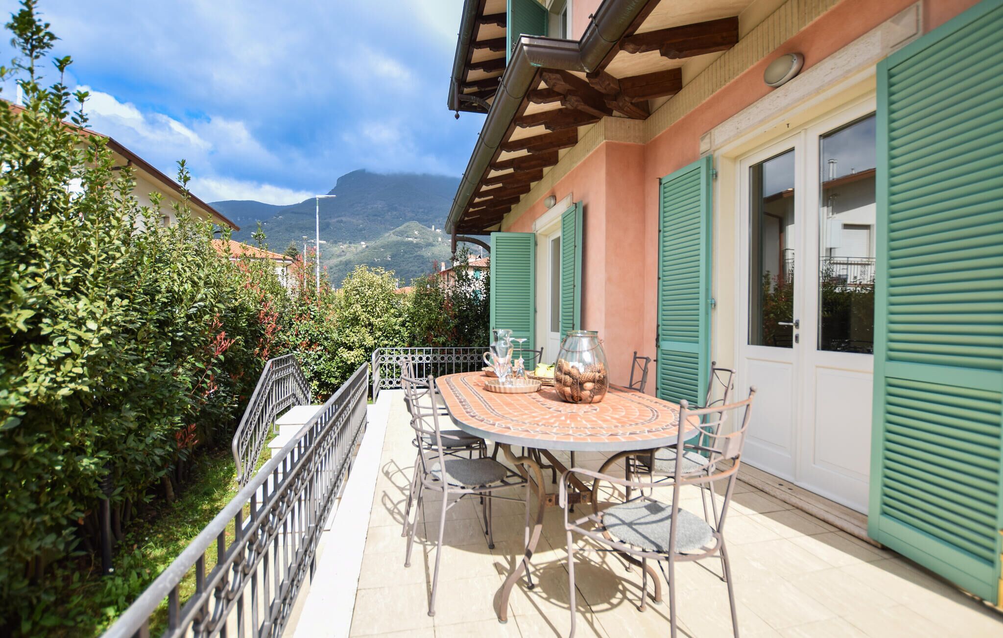 Patio esterno con tavolo e sedie rotonde, immerso nel verde e con vista sulle montagne.