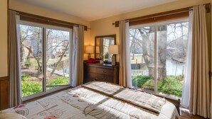 A bedroom with a large bed, a dresser, a mirror, and a view of a lake through large windows. - Chautauqua Lake Access: Waterfront Cottage w/ Dock (Mayville)