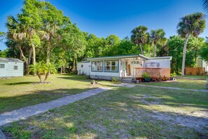 A small, single-story mobile home with a porch and a fenced yard, surrounded by trees. - Cozy Fort Pierce Cottage on Farm Animal Rescue! (Fort Pierce)