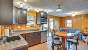 Una cocina con encimeras de granito, microondas integrado y lavavajillas. Hay una zona de comedor con una mesa de madera y cuatro sillas.