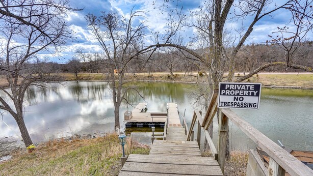 Una escalera de madera que lleva a un muelle sobre un lago tranquilo, rodeado de árboles y un letrero que dice 'PRIVATE PROPERTY NO TRESPASSING'.
