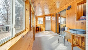 Interior de una cabaña de madera con un ventanal grande, una puerta, una mesita y un banco.