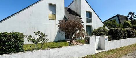 Una casa moderna de dos pisos con techo inclinado, una chimenea visible y un pequeño árbol en la parte delantera.