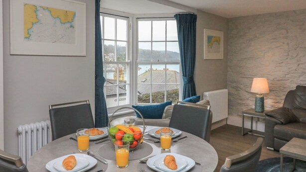 Un comedor con una mesa dispuesta para el desayuno, vista al mar a través de amplios ventanales y una pared de piedra.