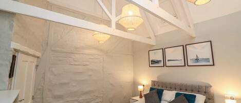 A bedroom with a bed, white walls, a stone accent wall, and three framed pictures on the wall.