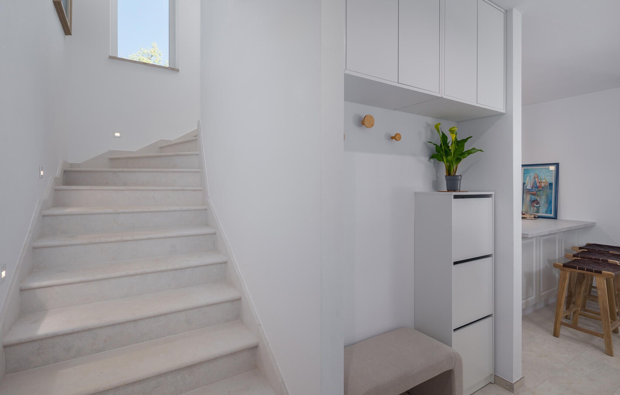 Una escalera que lleva a un rellano con una planta en maceta y un cuadro colgado en un armario blanco.