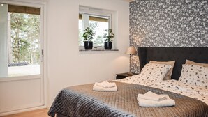 Ein Schlafzimmer mit einem Bett, zwei Nachttischen, einem Fenster mit Pflanzen und floralem Wandpapier.