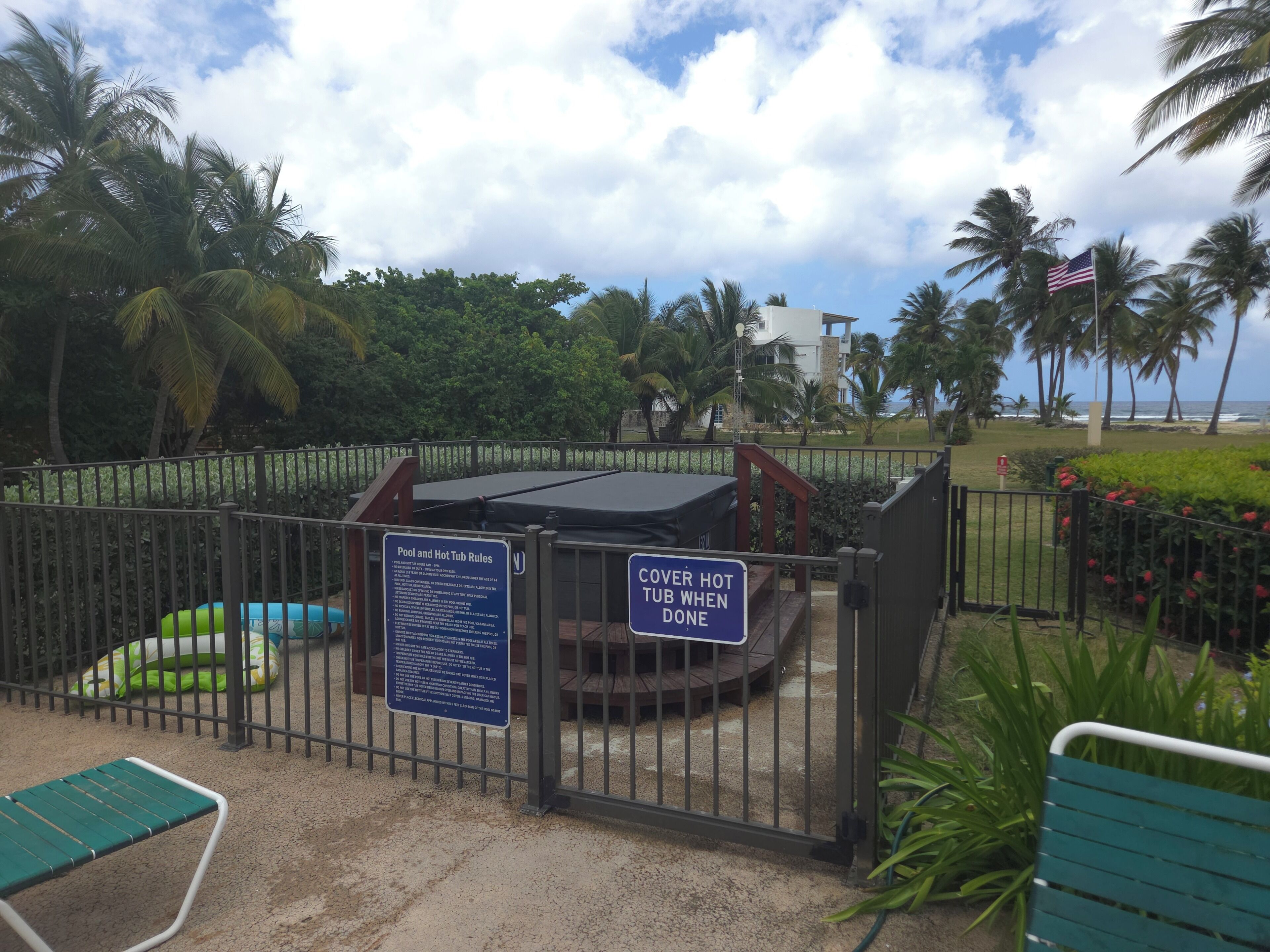Une piscine entourée d’une clôture, avec un jacuzzi extérieur, un jacuzzi couvert et un panneau indiquant les règles d’utilisation de la piscine et du jacuzzi.