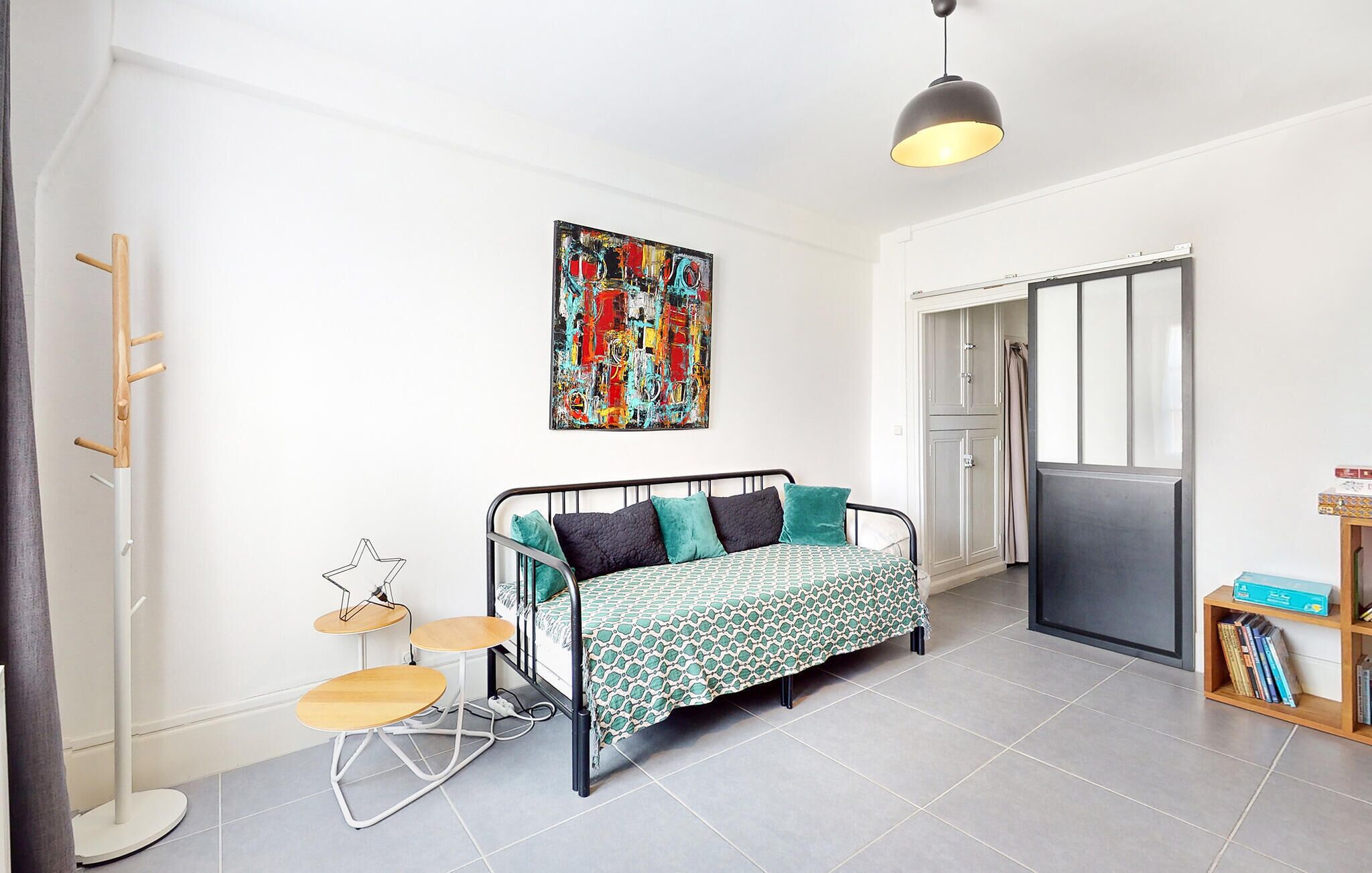 A compact bedroom with a bed, a small table, a chair, a coat rack, and a wardrobe.
