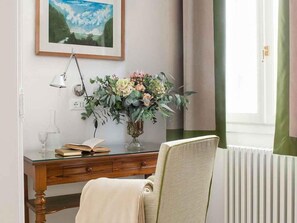 Een kamer met een houten bureau, een bloevas, een lamp en een lijst met een schilderij aan de muur.