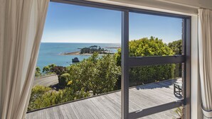 A room with a large window overlooking a coastal landscape, including a beach and a rocky outcrop.
