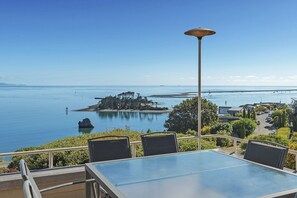 Une table entourée de chaises sur un balcon donnant sur la côte, avec une jetée et une petite île en vue.
