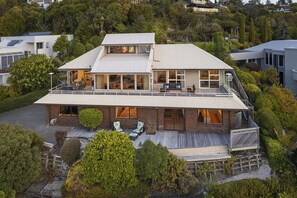 Une maison moderne à deux étages, dotée d’un grand balcon, d’une terrasse couverte et offrant une vue sur les arbres environnants.