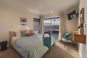 Une chambre d’hôtel comprenant un lit, un bureau, une chaise, une télévision et un balcon avec vue sur la mer.