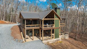 A two-story log cabin with a balcony and large windows, surrounded by a wooded area. - Eagles on the Ridge - Nearby River Access | Hot Tub | Game Room (Blue Ridge)