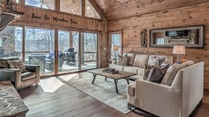 A cozy cabin interior with a large sliding glass door leading to an outdoor deck, a comfortable seating area with a sofa and armchairs, and a fireplace. - Eagles on the Ridge - Nearby River Access | Hot Tub | Game Room (Blue Ridge)