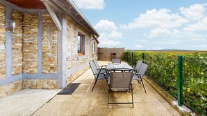 Un bâtiment en pierre doté d’un patio comprenant une table et des chaises, une fenêtre et une vue sur un champ verdoyant.