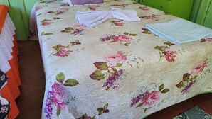 A bed with a floral bedspread and a folded white towel. - POUSADA CANTO DOS PÁSSAROS (Manaus)