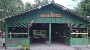 A green building with a sign reading "Centro De Sitio De Turismo Kamela" and two colorful parrots perched on the roof. - POUSADA CANTO DOS PÁSSAROS (Manaus)