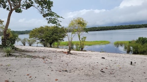 A sandy beach with trees and a calm lake. - POUSADA CANTO DOS PÁSSAROS (Manaus)