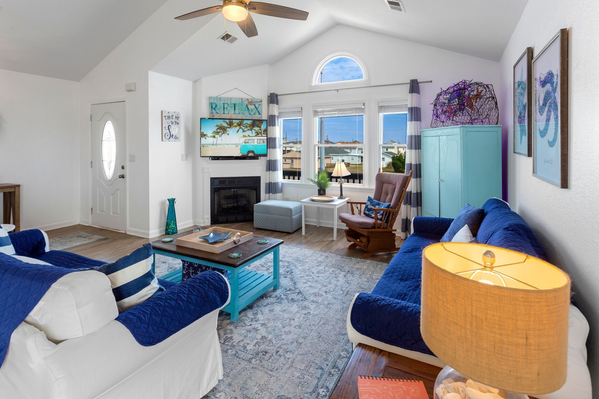 A cozy living room with a fireplace, a teal cabinet, and a large window with a view of houses.