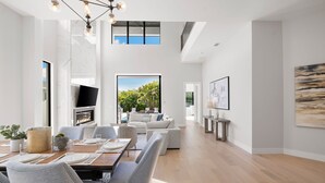 A modern interior with a dining area, a living room with a sofa and TV, and a large window with a view of greenery. - NEW Villa Mare LUX Sleeps 12 l Heated Pool l 2 Masters (Naples)