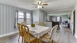 Un coin repas avec une table dressée pour quatre personnes, des chaises en bois, un ventilateur de plafond et une vue par la fenêtre.