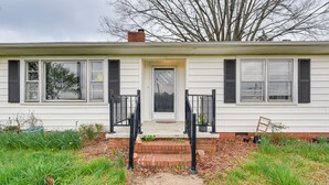 Une maison de plain-pied avec une porte d’entrée, deux fenêtres avec volets, un petit porche et des fondations en briques.