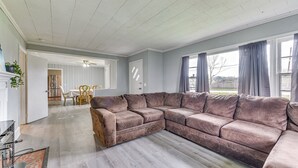 Un vaste salon doté d’un grand canapé d’angle, d’un coin repas avec une table et des chaises, et offrant une vue sur l’extérieur grâce à de grandes fenêtres.