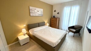 Un dormitorio con cama, mesitas de noche, una silla, cómoda y un cuadro en la pared.
