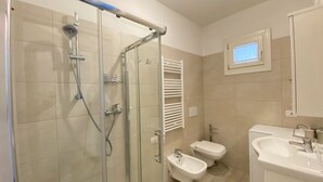 Un baño moderno con ducha de vidrio, un bidé, inodoro y lavamanos.