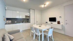 Una cocina moderna con armarios blancos, una mesa de comedor con sillas, un televisor montado en la pared y un sofá en la sala.