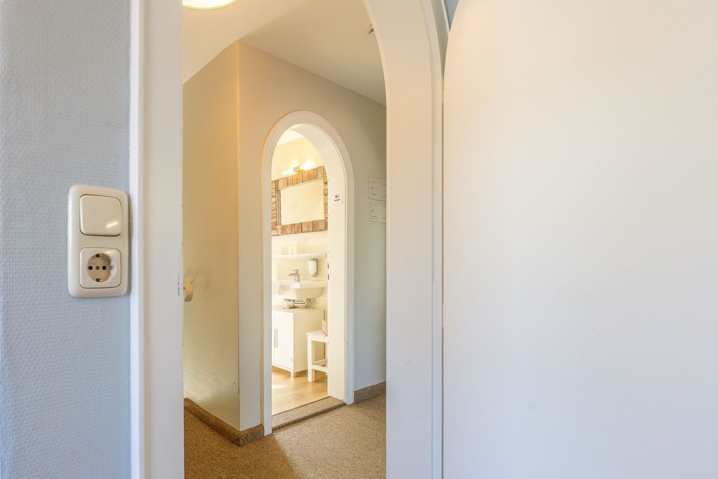 A hallway leading to a bathroom with a white sink and a mirror above it.