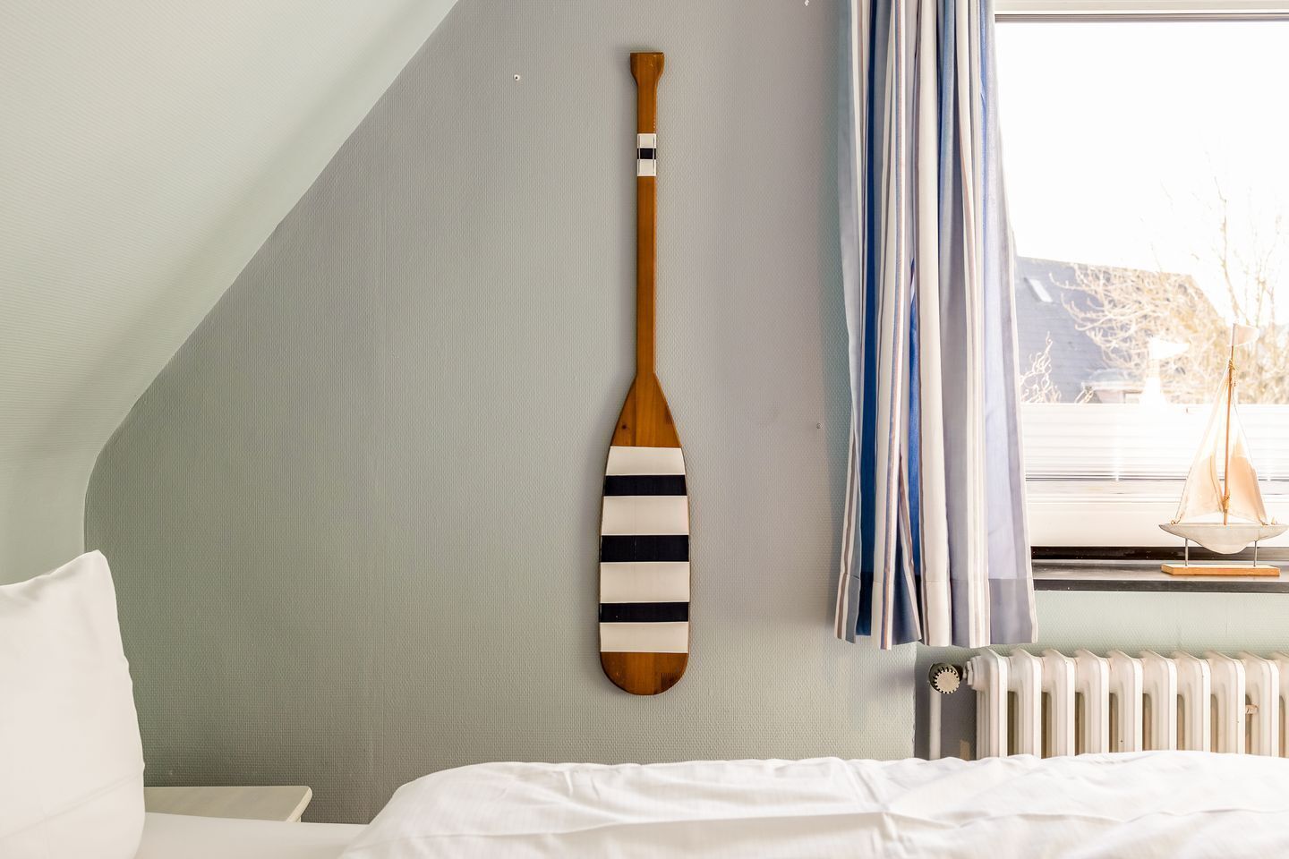 A room with a bed, a wall-mounted paddle, a window with curtains, and a radiator.