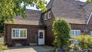 Een bakstenen huis met pannendak, een voordeur en een kleine tuin met stenen en planten.