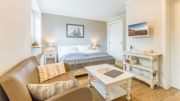 Een gezellig slaapkamer met een bed, nachtkastje, lamp, televisie en een klein tafeltje met een laptop.