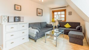 A cozy living room with a grey sofa, a glass coffee table, and a white dresser with drawers. - Sylt Homes Auster 4 - Appartement Auster No.4 (Sylt)
