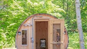 Una cabaña de madera con la puerta abierta, mostrando un interior pequeño con un calentador y una ventana.