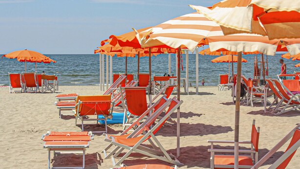 A beach with rows of orange and white striped beach umbrellas and orange lounge chairs.