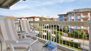 A balcony with white chairs and a table, overlooking a residential area with buildings and greenery.