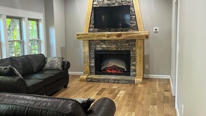 A living room with a stone fireplace, a ceiling fan, and a large window. - Merlot- 2 bedroom Cottages near Jones von Drehle (Thurmond)