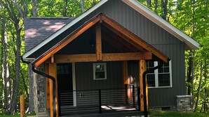 A cabin with a stone foundation, a wooden porch, and a metal railing. - Merlot- 2 bedroom Cottages near Jones von Drehle (Thurmond)