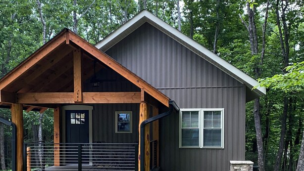 A two-story cabin with a wooden deck and stone foundation, surrounded by lush greenery. - Merlot- 2 bedroom Cottages near Jones von Drehle (Thurmond)