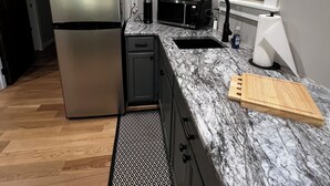 A modern kitchen with a stainless steel refrigerator, a microwave, a sink, and a wooden cutting board on the counter. - Merlot- 2 bedroom Cottages near Jones von Drehle (Thurmond)