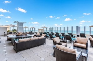 A rooftop terrace with outdoor seating, a fire pit, and a view of the ocean.