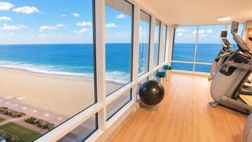 Une salle de sport équipée de matériel d’exercice et dotée d’une grande fenêtre donnant sur une plage.