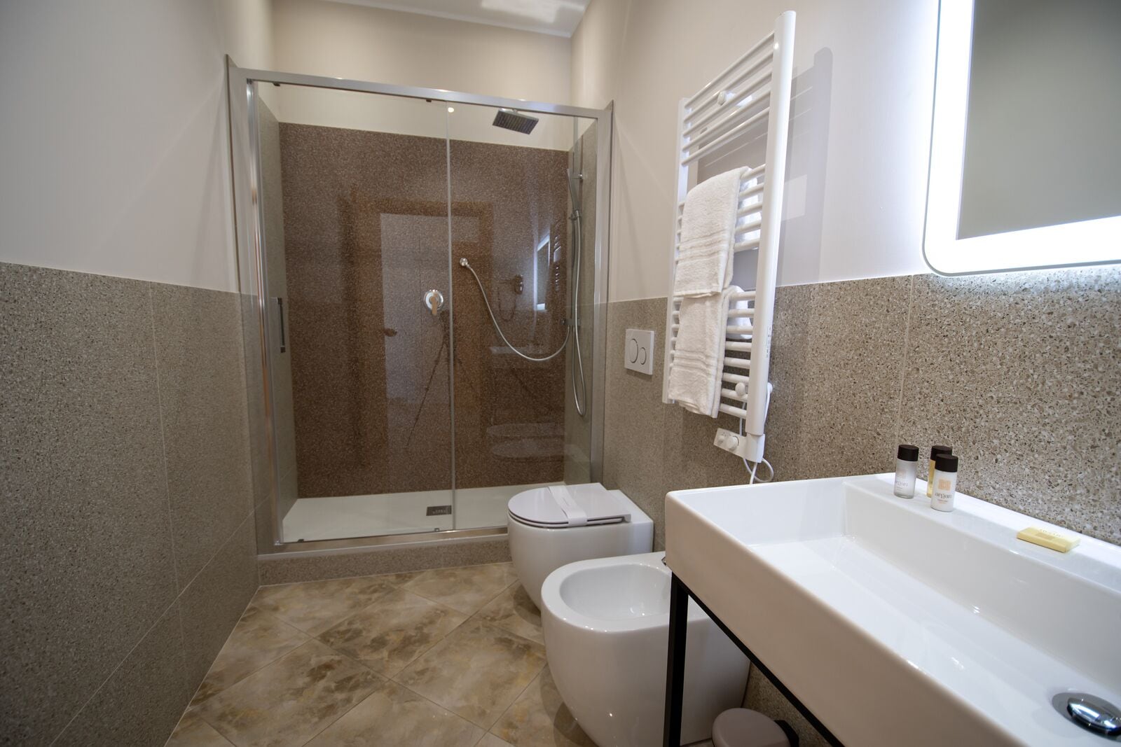 A modern bathroom with a glass-enclosed shower, a toilet, and a sink with toiletries.
