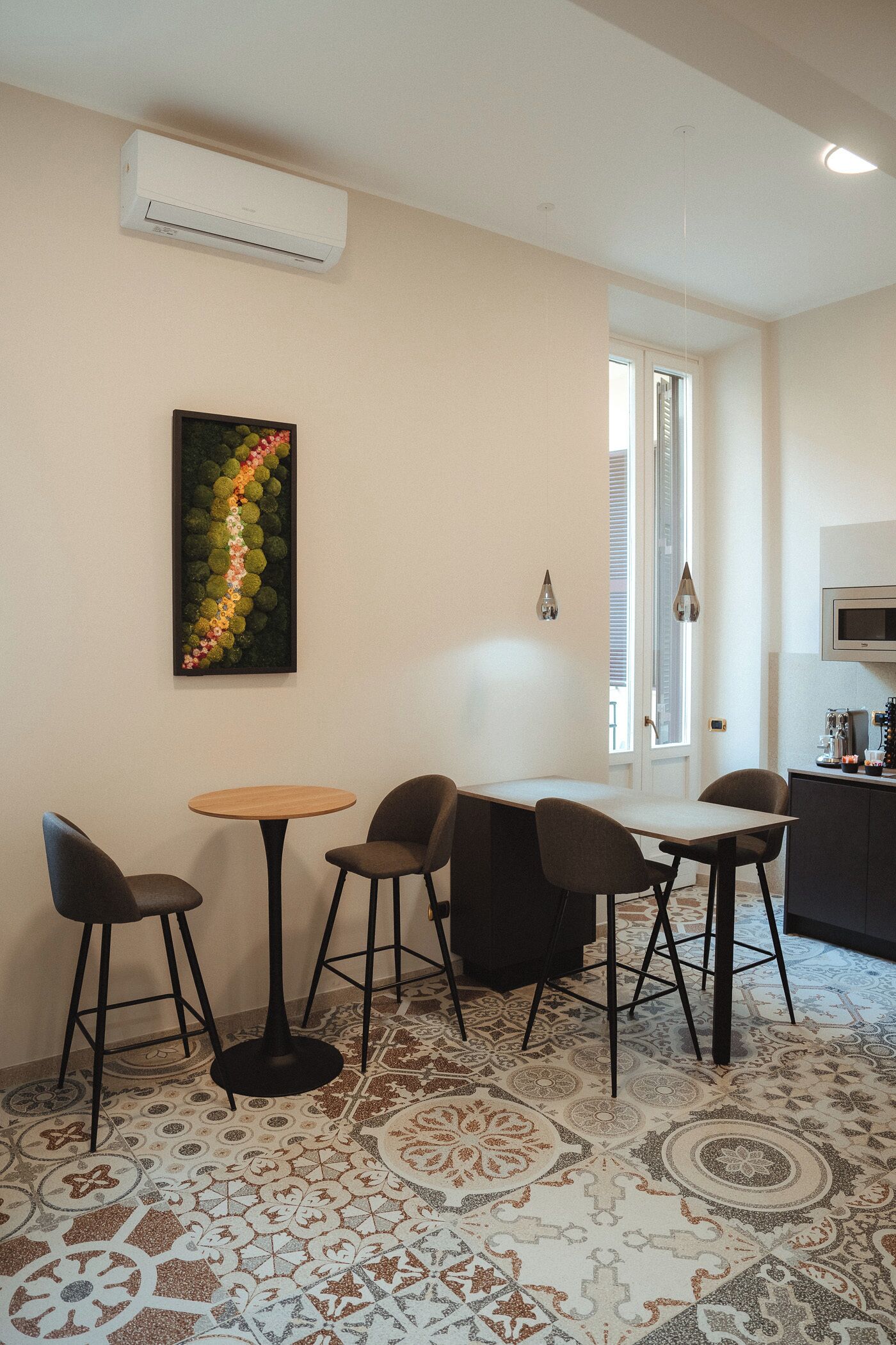 A dining area with a round table and four chairs, a decorative wall piece, and an air conditioning unit above.