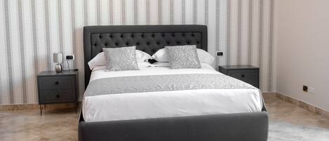 A modern bedroom with a large bed, two bedside tables, and a striped wallpaper background.