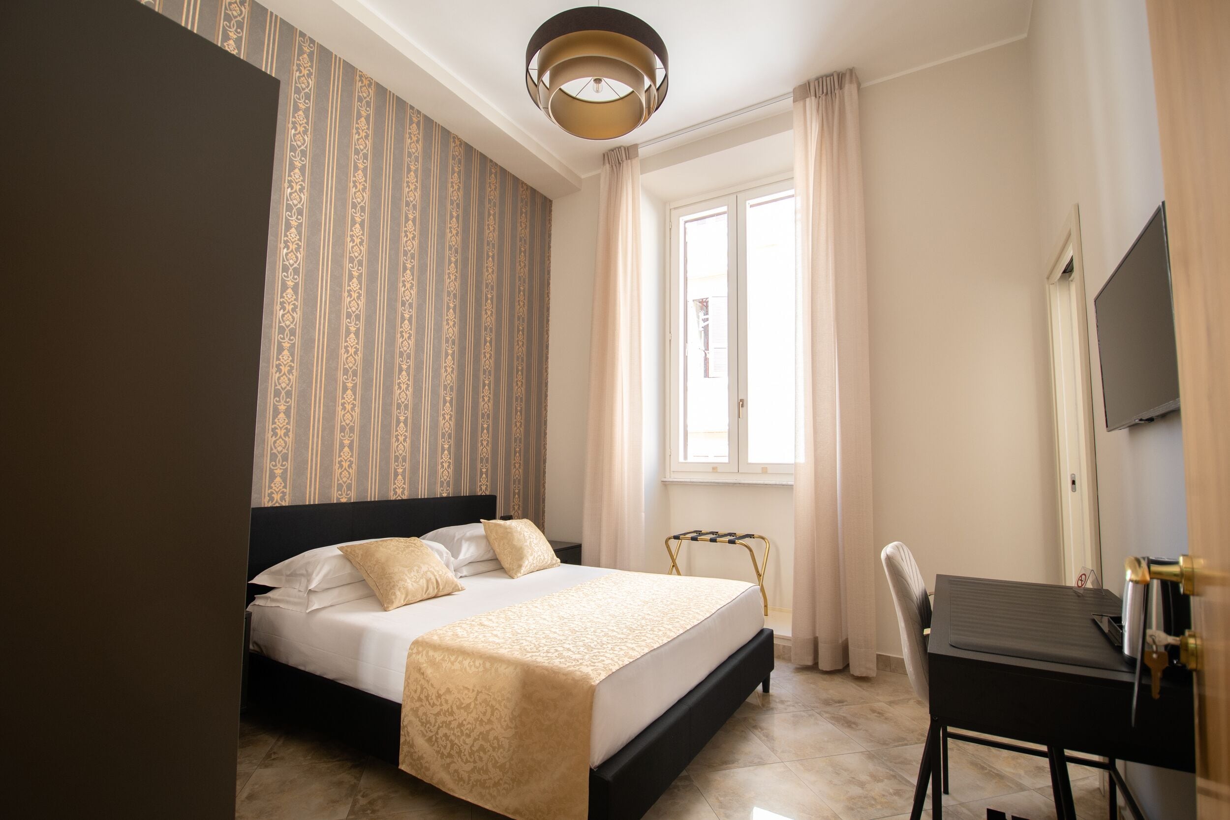 Una habitación de hotel con cama, escritorio, silla, televisión y ventana con cortinas.